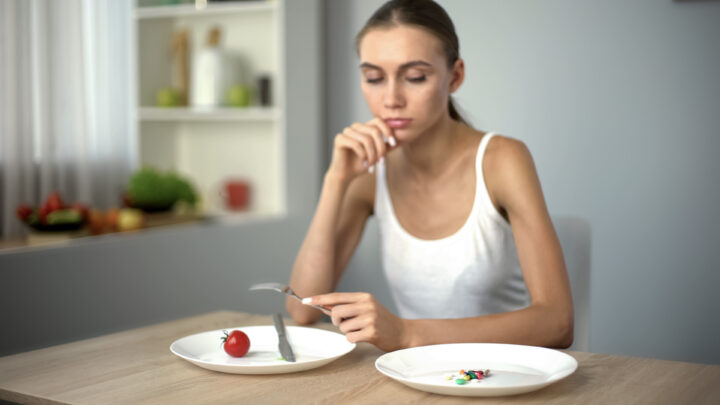 Thin girl looking at anti-obesity pills, obsession with weight loss, addiction