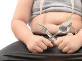 Overweight boy holding fork and spoon isolated over white, diet to lose weight and healthy concept