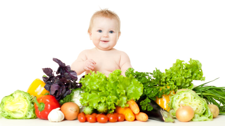 The babe in an environment of the fresh vegetables, isolated on the white