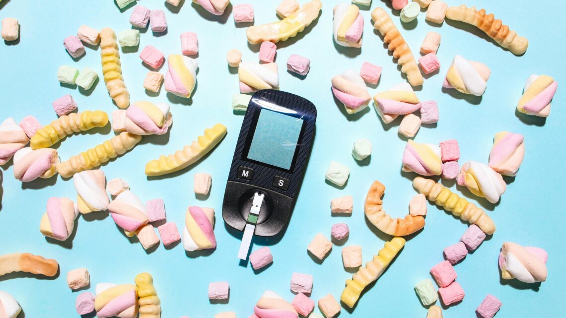 Glucose meter surrounded by sweet treats on a blue surface