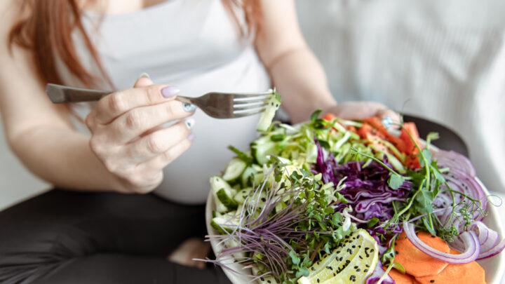 Close-up of a plate with a bright salad of fresh vegetables in the hands of a pregnant woman.