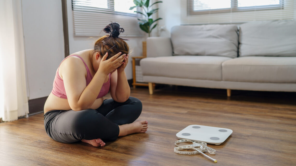 Obese Woman with fat upset bored of dieting Weight loss fail Fat diet and scale sad asian woman on weight scale at home weight control.