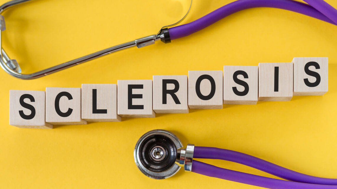 sclerosis word written in wooden blocks on yellow table with stethoscope. Medicine, health and wellbeing concept