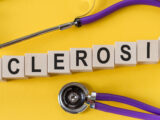 sclerosis word written in wooden blocks on yellow table with stethoscope. Medicine, health and wellbeing concept