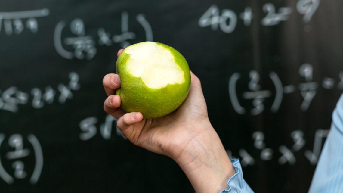 Sweet lesson: Girl with an apple - a symbol of health and education against the backdrop of a school blackboard.