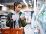 Young woman buying diary product and reading food label in grocery store.