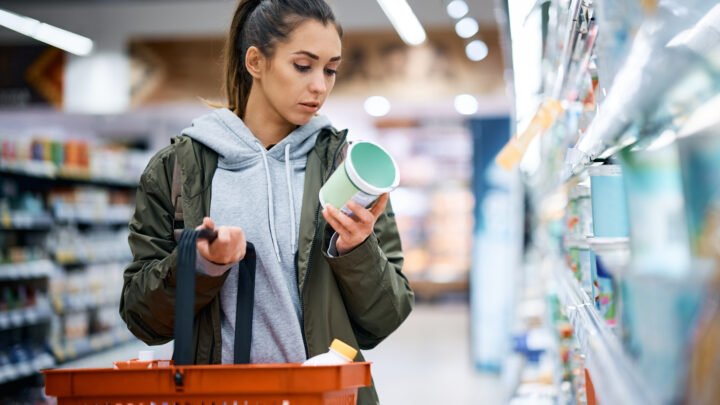 Young woman buying diary product and reading food label in grocery store.